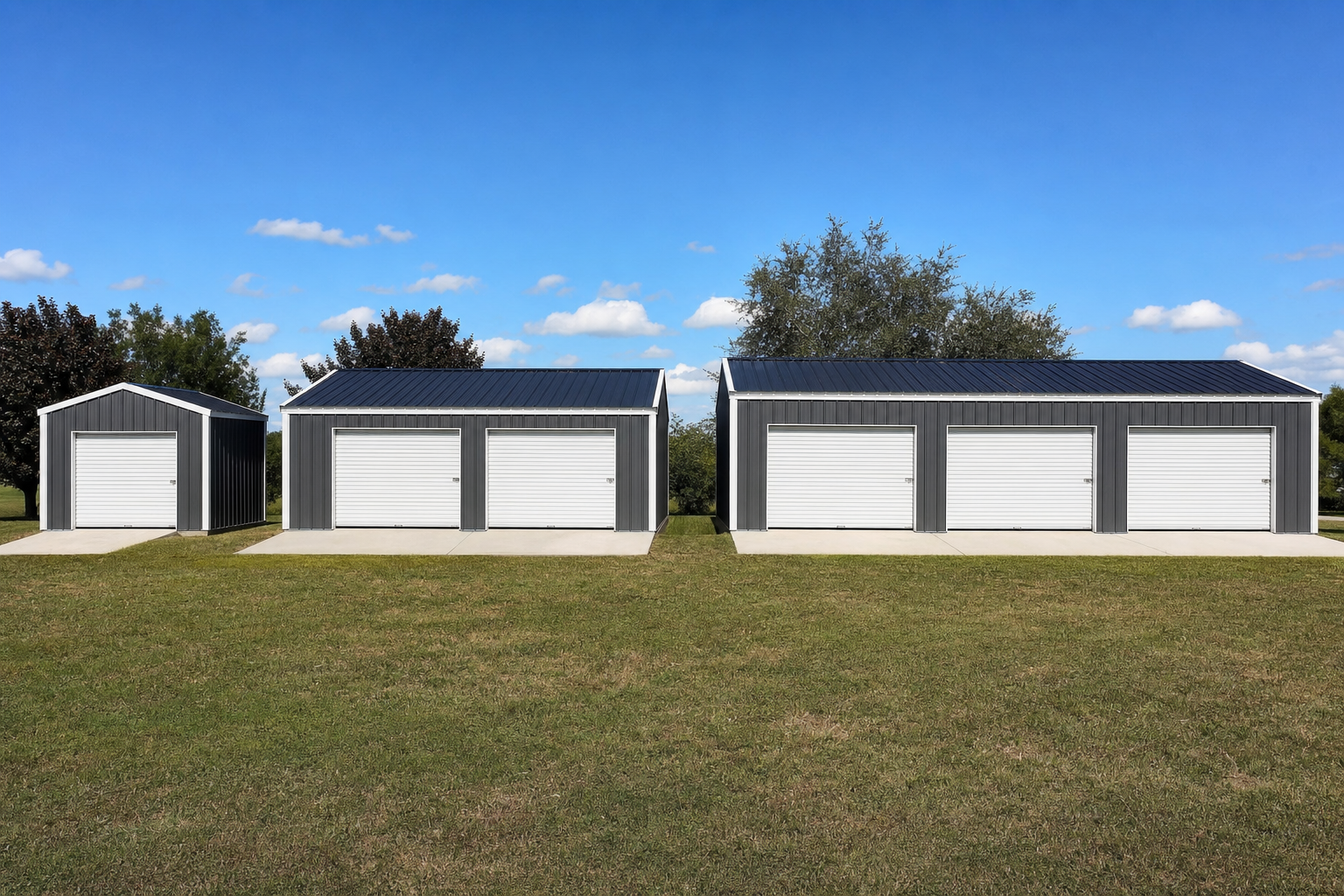 Three gray metal garages with white roll-up doors stand side by side on a grassy lawn under a blue sky with scattered clouds. Trees are visible in the background.